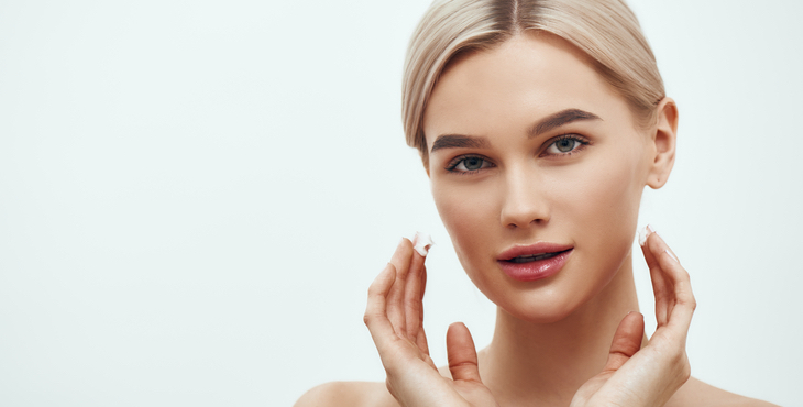 Horizontal web banner. Beautiful young blonde woman touching her face and looking at camera while standing against grey background. Skin care. Beauty concept